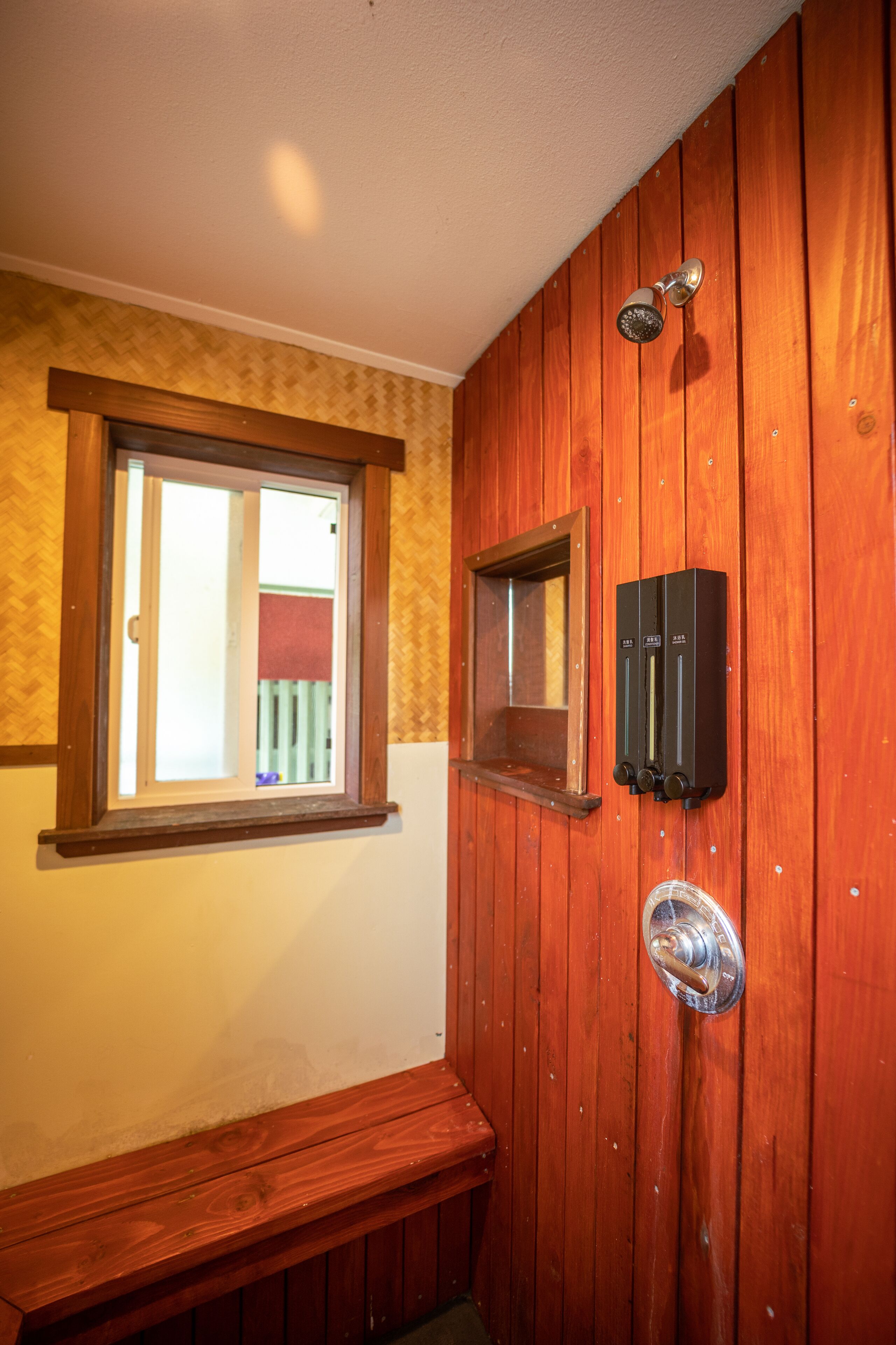 A wooden bathroom with a bench, a window, and a showerhead.