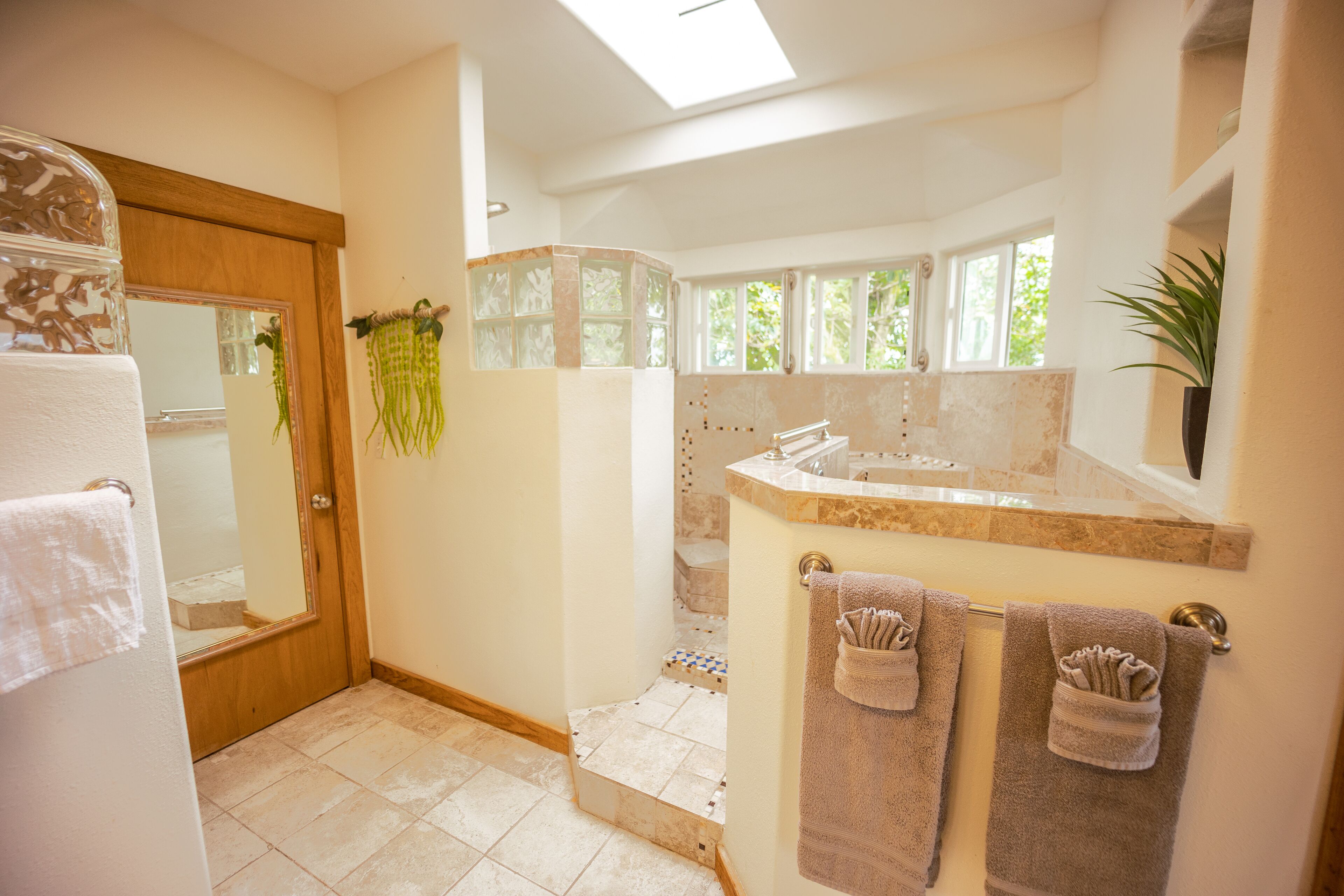 A bathroom with a shower, a sink, and a mirror. There are towels hanging on the wall and a plant on the counter.