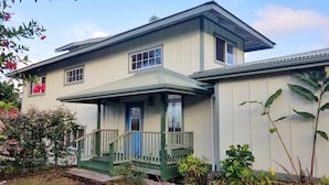 A two-story house with a porch, a blue door, and a small garden.