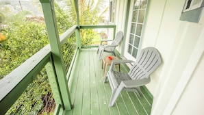 A porch with green railings, two white plastic chairs, and a small table with a red object on it.