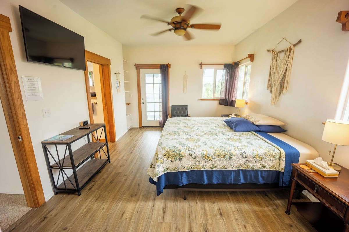 Un dormitorio con cama, escritorio, ventilador de techo, ventana y puerta.