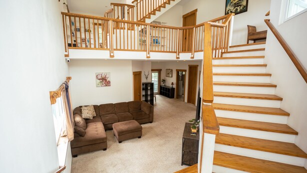 A spacious living area with a large brown sectional sofa, a wooden staircase, and a high ceiling with skylights.