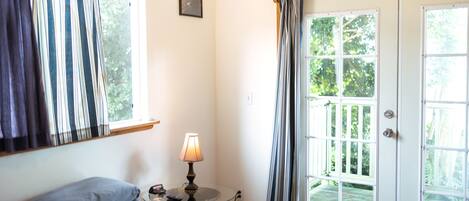 Un dormitorio con cama, mesita de noche con lámpara, ventana con cortinas y puerta que da a un espacio exterior.