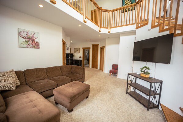 A spacious living room with a brown sectional sofa, a wooden console table, and a flat-screen TV mounted on the wall.