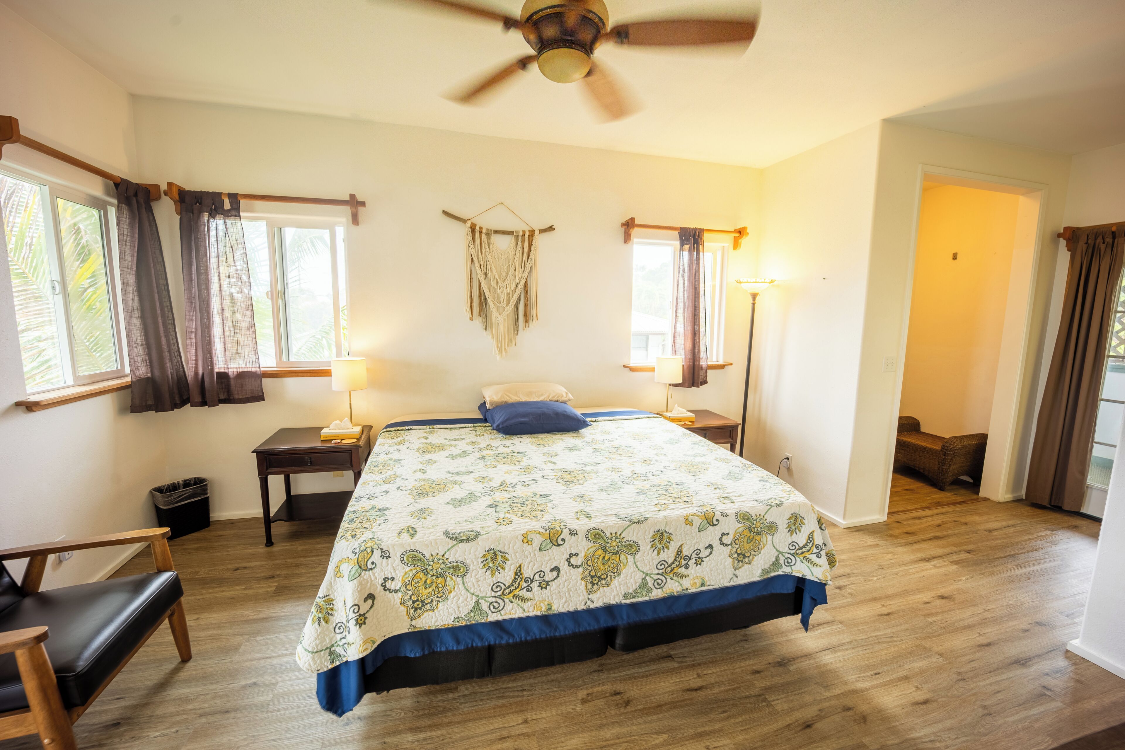A bedroom with a bed, a ceiling fan, a bedside table, a lamp, a chair, and a window with curtains.