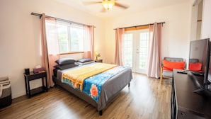 A bedroom with a bed, a television, a ceiling fan, and a window with curtains.