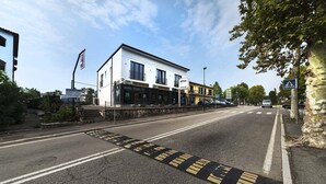 A modern building with a storefront, a pedestrian crossing, and a clear road. - Garda Room (Peschiera del Garda)