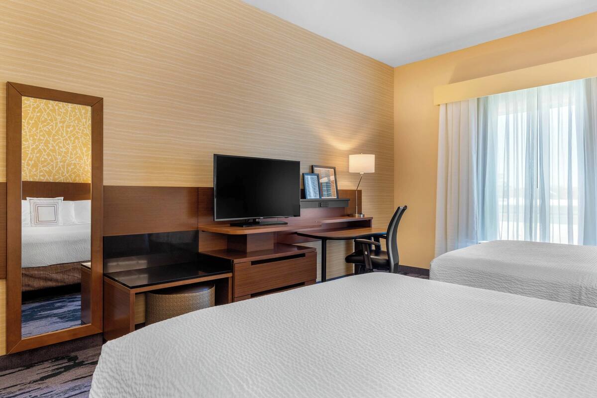 A hotel room with a large bed, a TV, a desk with a chair, a lamp, and a window with curtains.