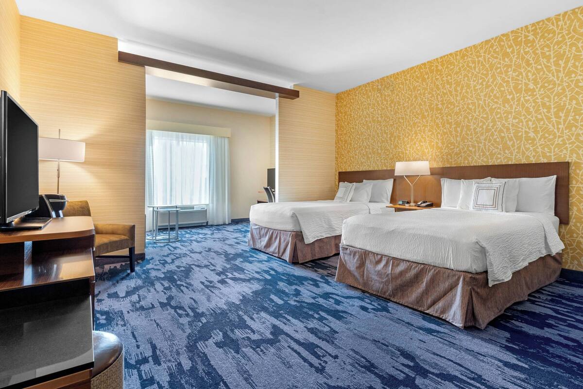 A hotel room with two beds, a TV, a desk, and a large window.