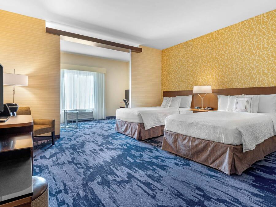 Une chambre d’hôtel avec deux lits, une télévision, un bureau et une grande fenêtre.