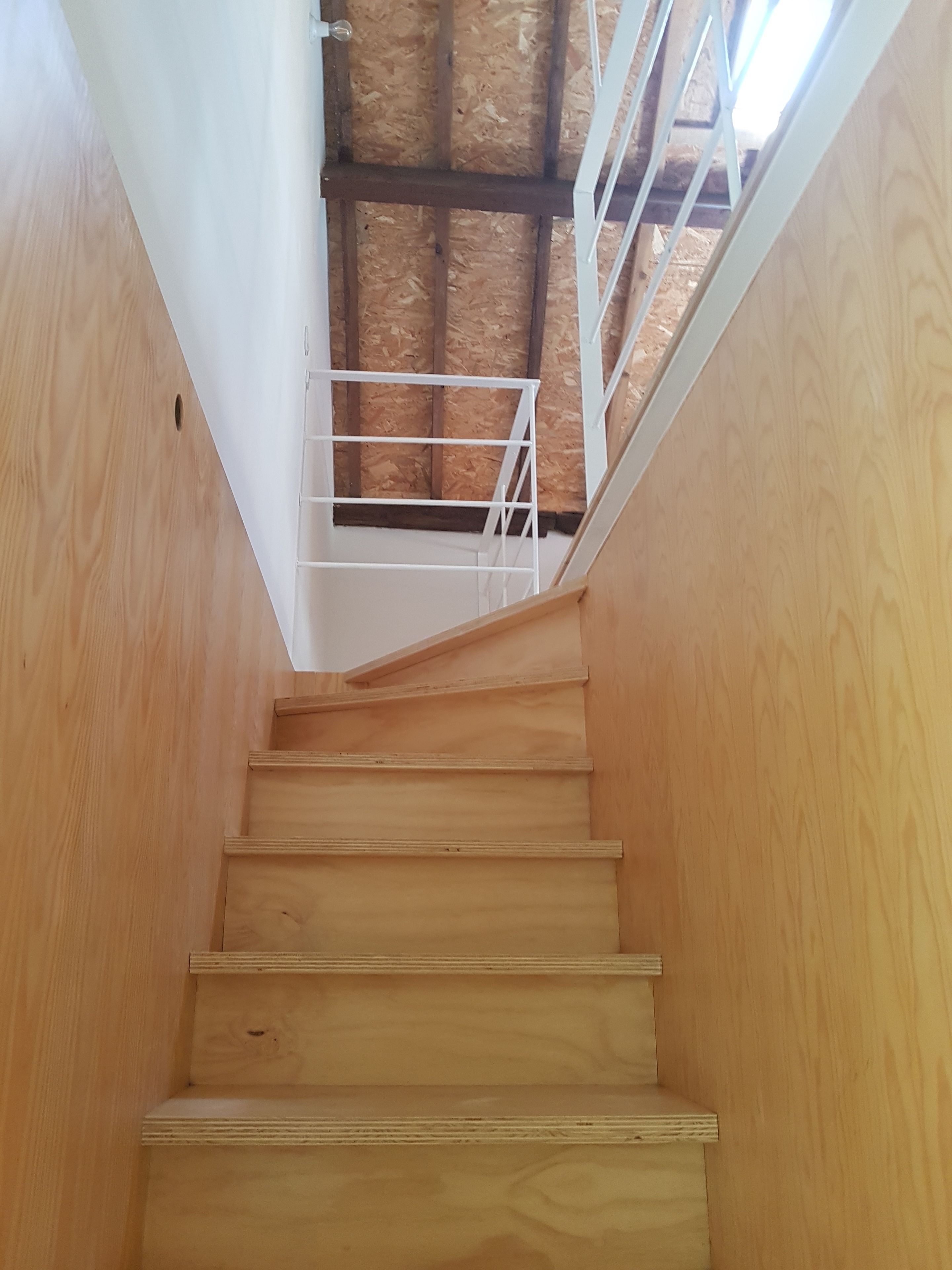 A wooden staircase with white railings leading to a ceiling with wooden beams.