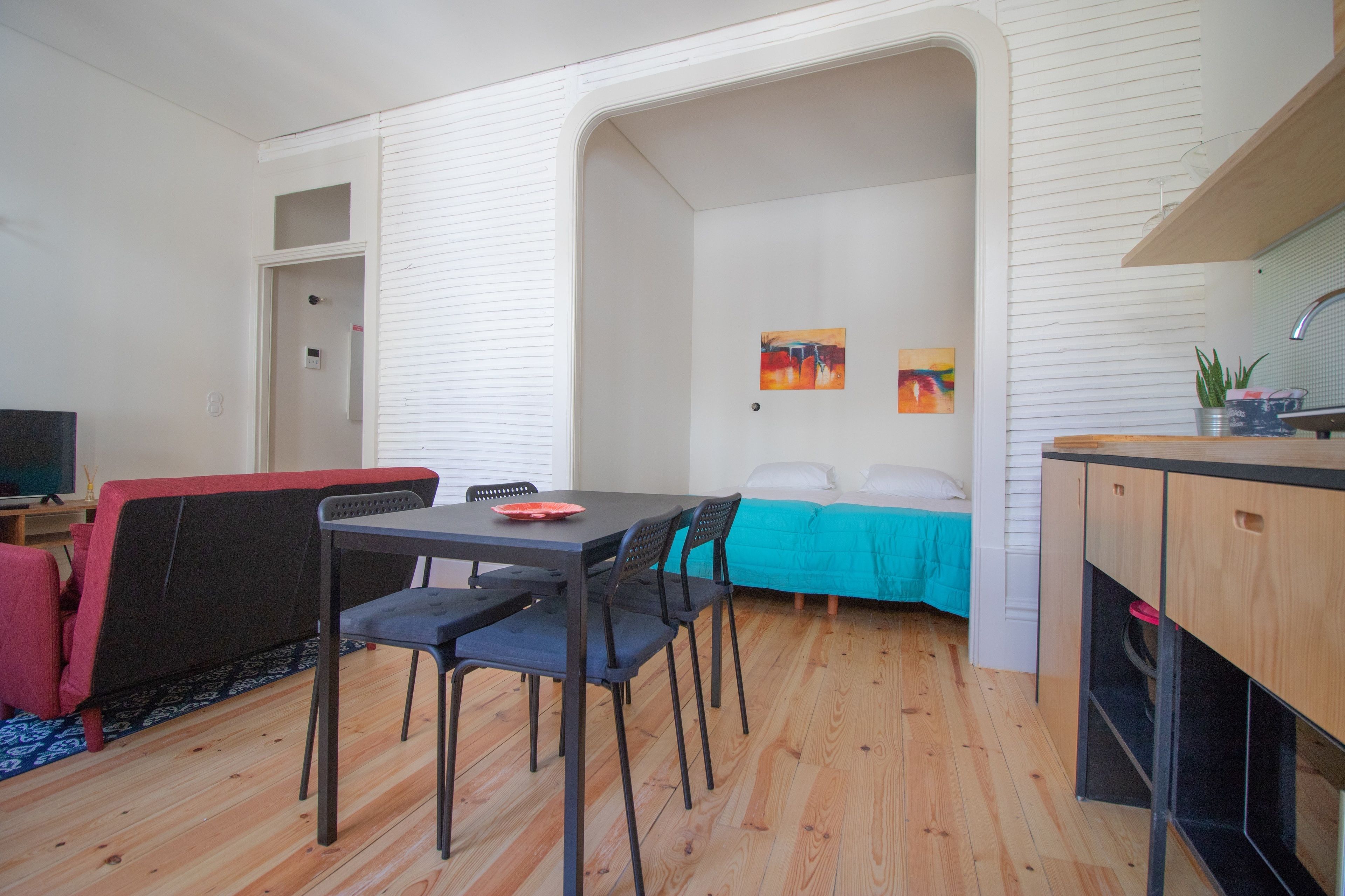 A compact living space with a dining area, a kitchenette, a sofa, and a bed.