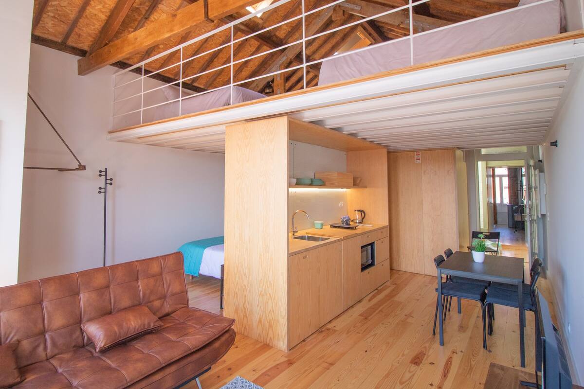 A loft-style room with a wooden ceiling, a kitchenette, a dining area, and a sofa.
