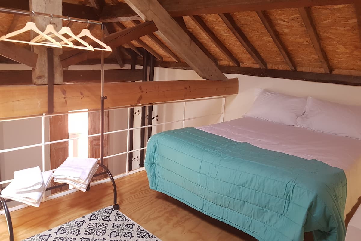 A rustic room with a wooden ceiling, a bed with teal bedding, a hanging clothes rack, and a patterned rug.