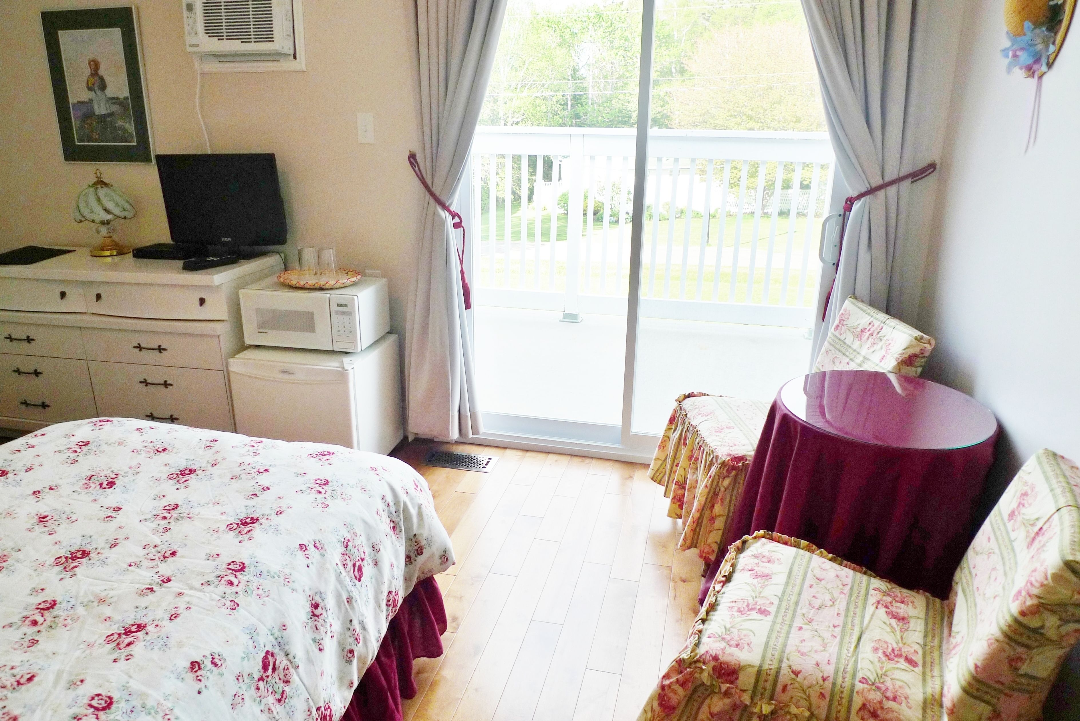A bedroom with a bed, a desk with a computer, a microwave, and a balcony with a table and chairs.