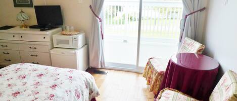 A bedroom with a bed, a desk with a computer, a microwave, and a balcony with a table and chairs.