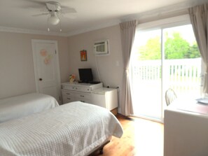 A bedroom with two beds, a desk, a chair, a ceiling fan, and a window with curtains.