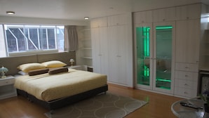Un dormitorio con una cama grande, una mesita de noche, un armario y un closet con puertas de vidrio iluminado en verde.