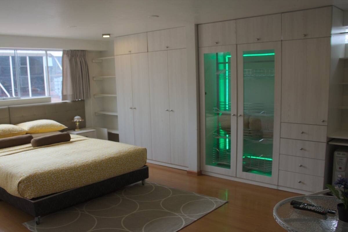 Ein Schlafzimmer mit einem großen Bett, einem Nachttisch, einem Kleiderschrank und einem Glastrennschrank mit grüner Beleuchtung.