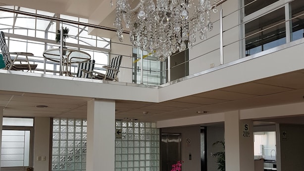 Un interior espacioso de dos pisos, con un candelabro, un comedor con sillas y mesas, y ventanas amplias.