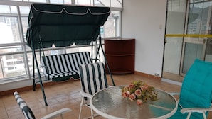 Un patio iluminado por el sol con una mesa redonda de vidrio, sillas a rayas y una silla color turquesa.
