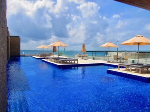 A rooftop infinity pool with lounge chairs and umbrellas, overlooking the ocean.