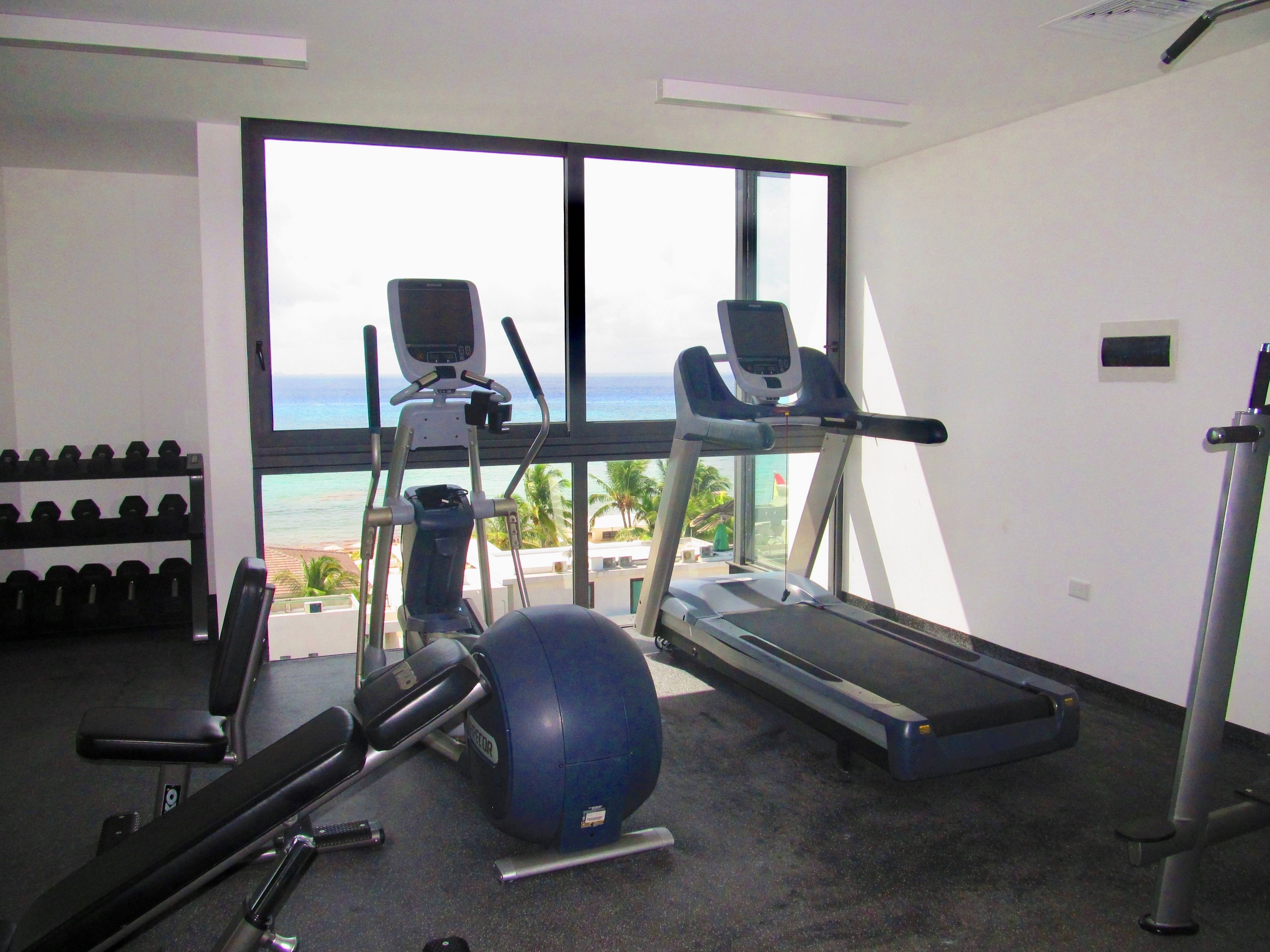 Een fitnessruimte met loopbanden, een elliptische trainer, gewichten en een hometrainer.