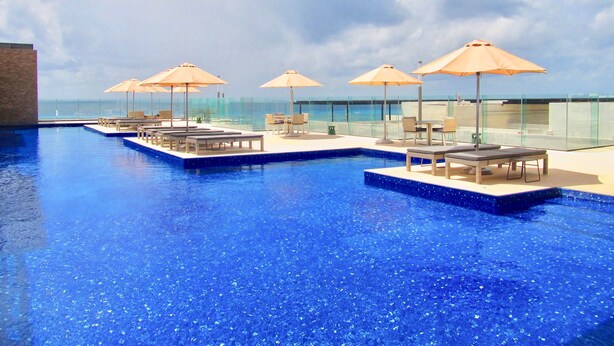 A rooftop infinity pool with lounge chairs and umbrellas, overlooking the ocean. - Cruz con Mar by Playa Paradise (Playa del Carmen)