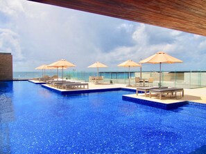 Ein Infinity-Pool auf dem Dach mit Liegestühlen und Sonnenschirmen, mit Blick auf den Ozean.