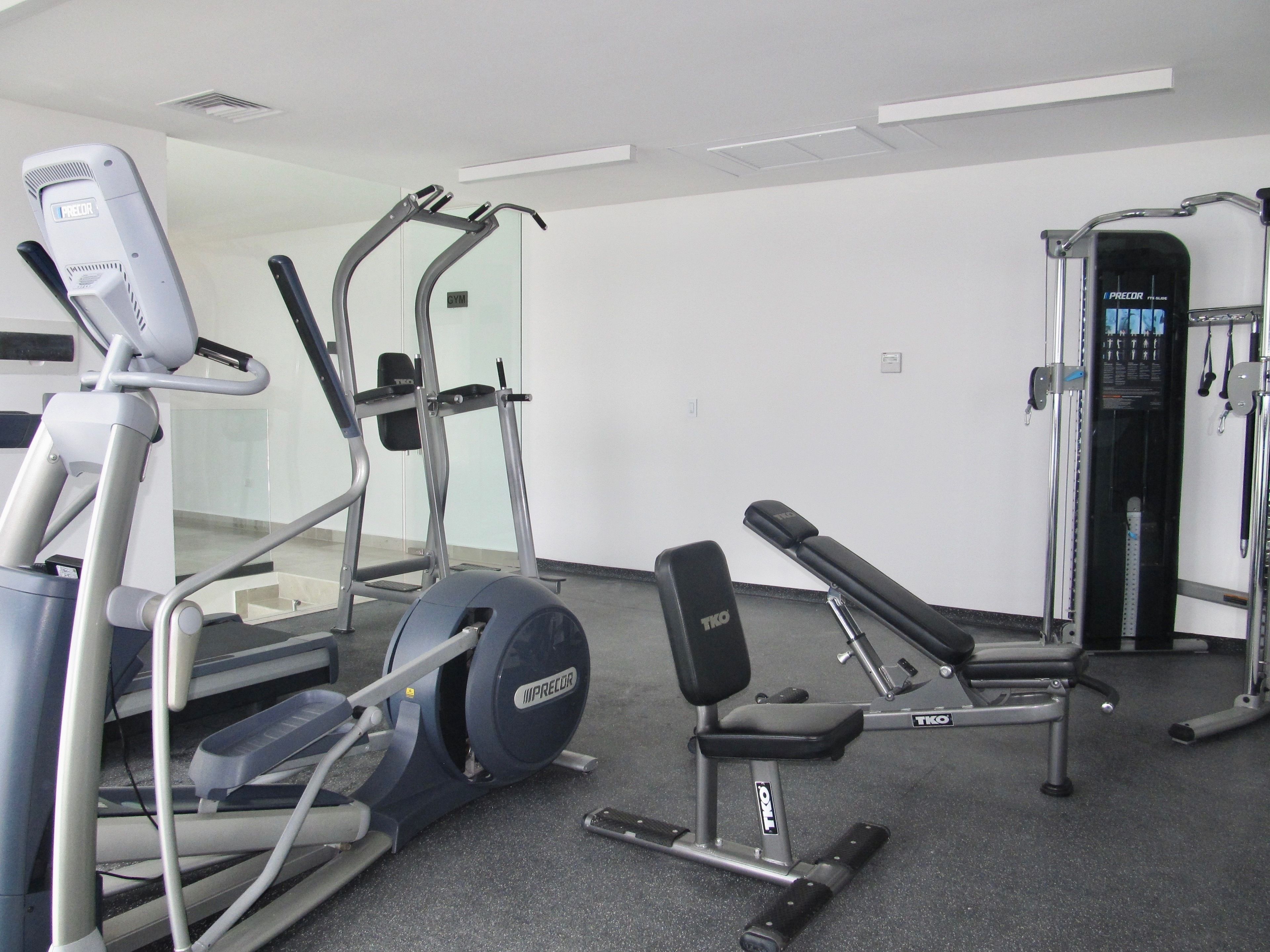 Une salle de sport équipée de machines de cardio, d’un banc de musculation et d’une machine à câbles.
