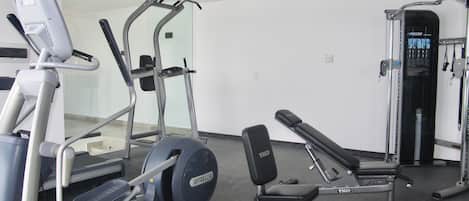 Une salle de sport équipée de machines de cardio, d’un banc de musculation et d’une machine à câbles.