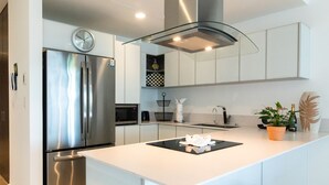 A modern kitchen with stainless steel appliances, a central island, and a clock on the wall. - Cruz con Mar by Playa Paradise (Playa del Carmen)