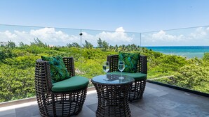 A balcony with wicker chairs and a glass table, overlooking a lush green landscape and a clear blue sky. - Cruz con Mar by Playa Paradise (Playa del Carmen)