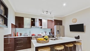 Een moderne keuken met een centraal eiland, barstoelen, een ingebouwde oven en een flatscreen televisie aan de muur.