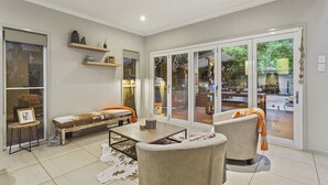 Een moderne woonkamer met een bank, fauteuils, een salontafel en een glazen schuifdeur naar een buitenruimte.
