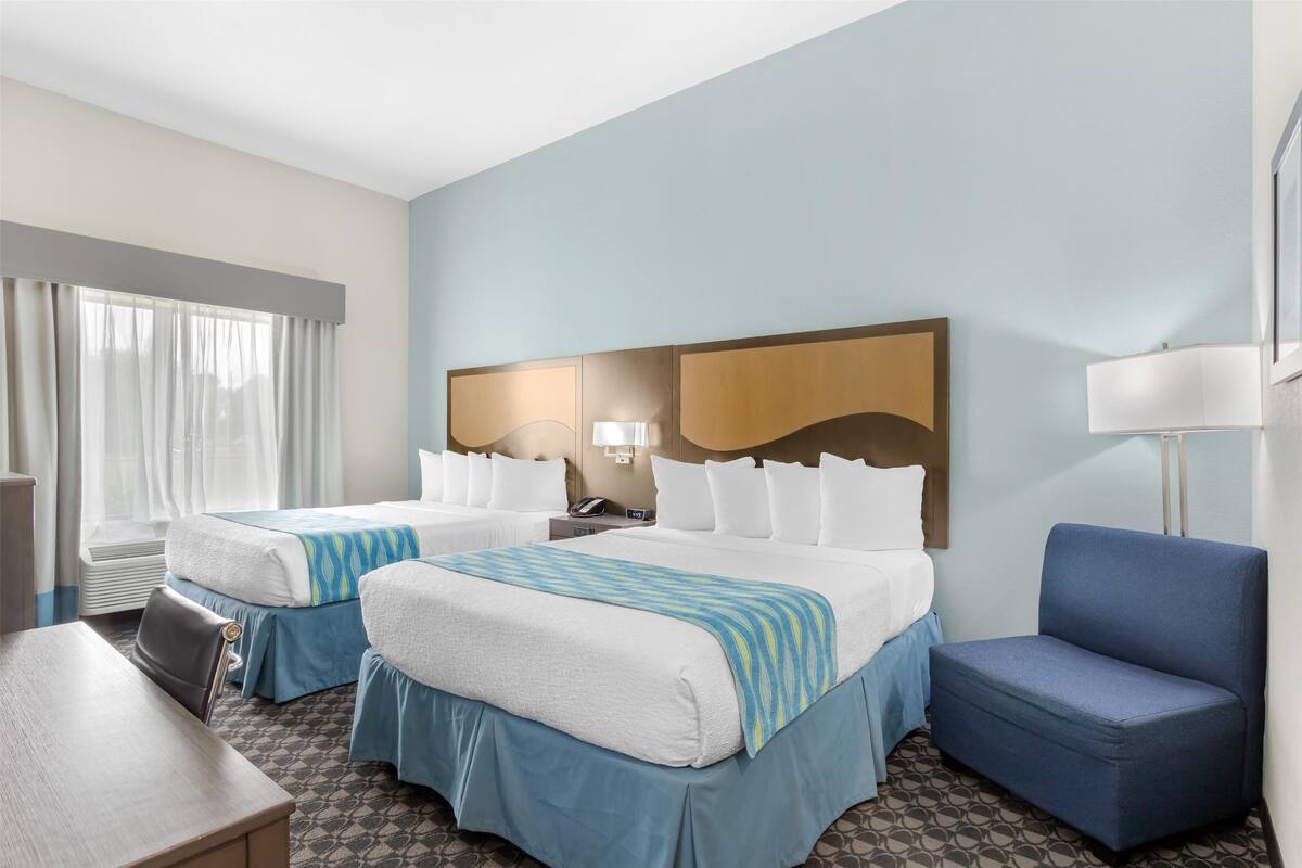 Habitación de hotel con dos camas, un escritorio, una silla y un ventanal con cortinas.