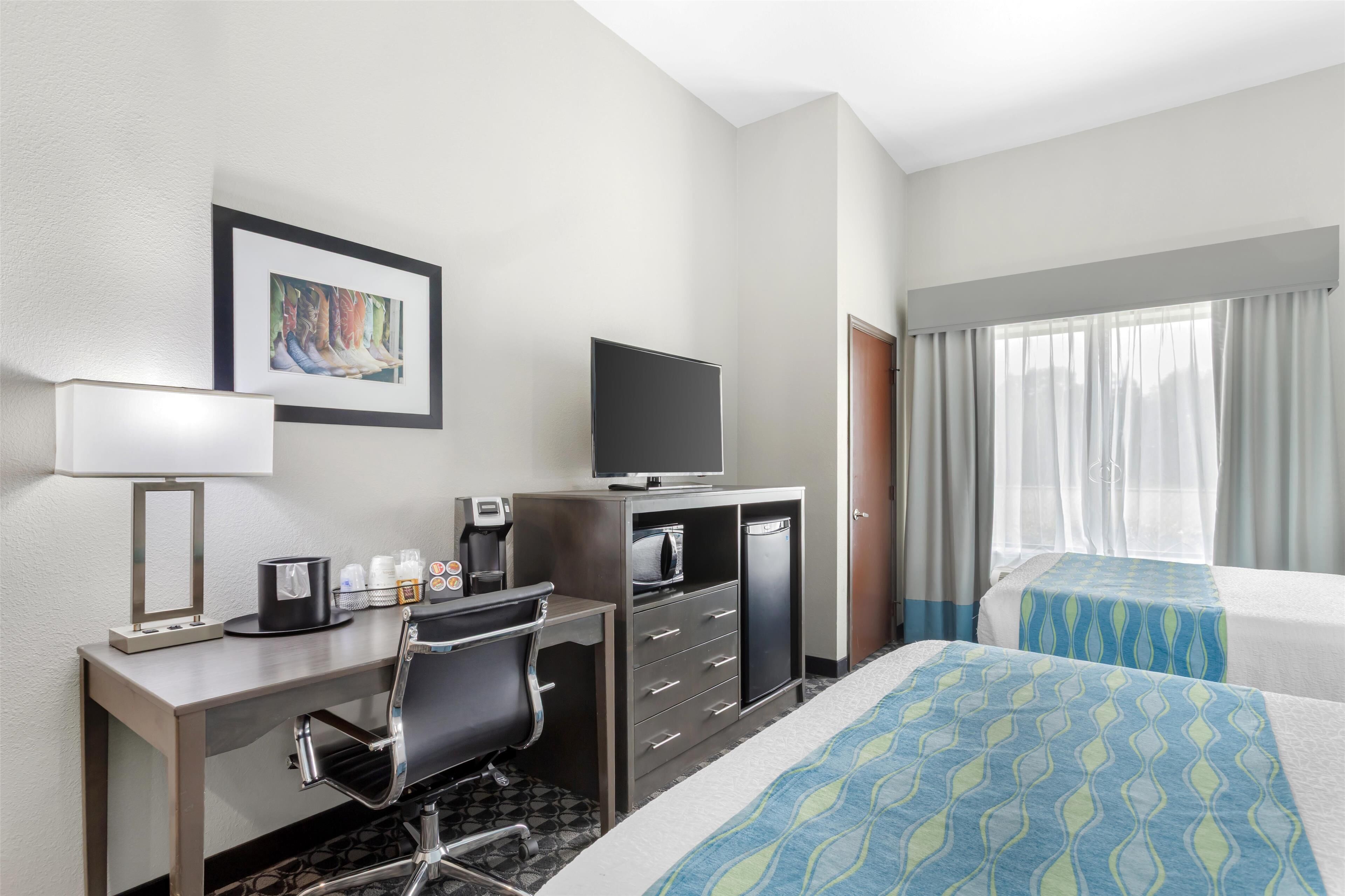 A hotel room with a desk, chair, television, minibar, and two beds with blue patterned bedspreads.