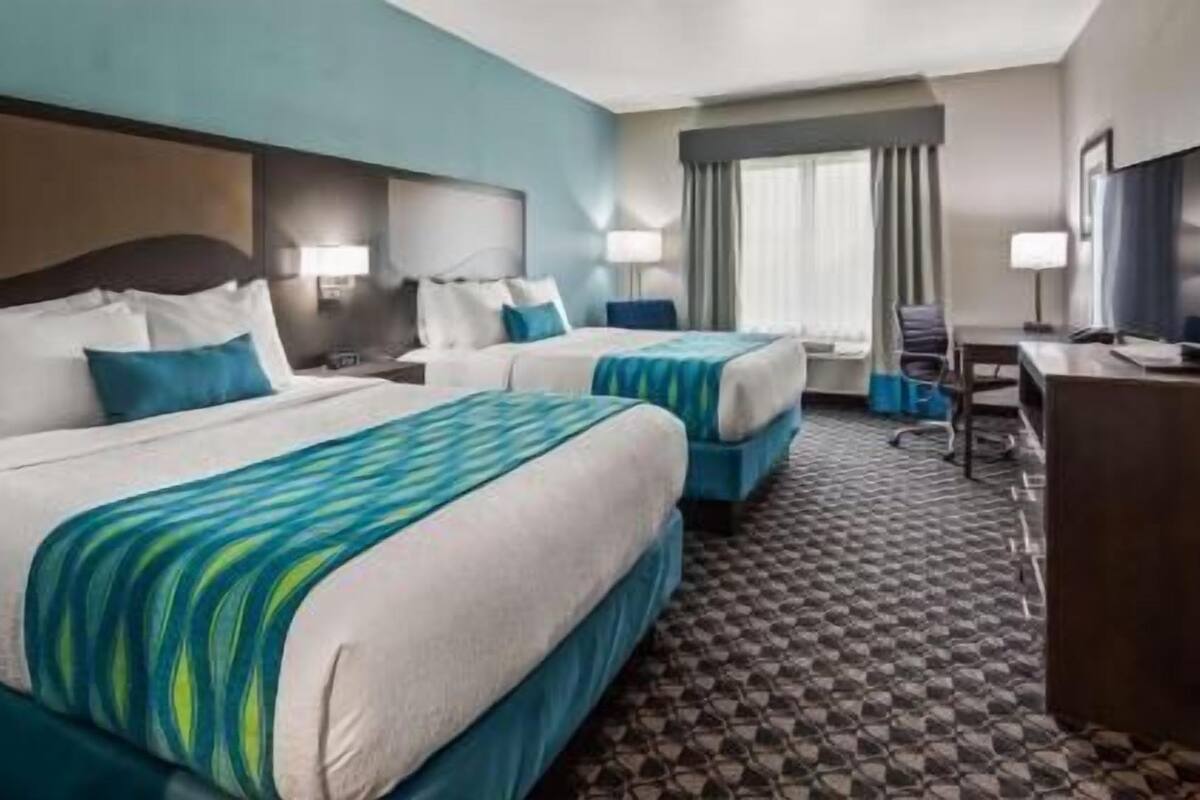 Habitación de hotel con dos camas, un escritorio, una silla y un televisor.