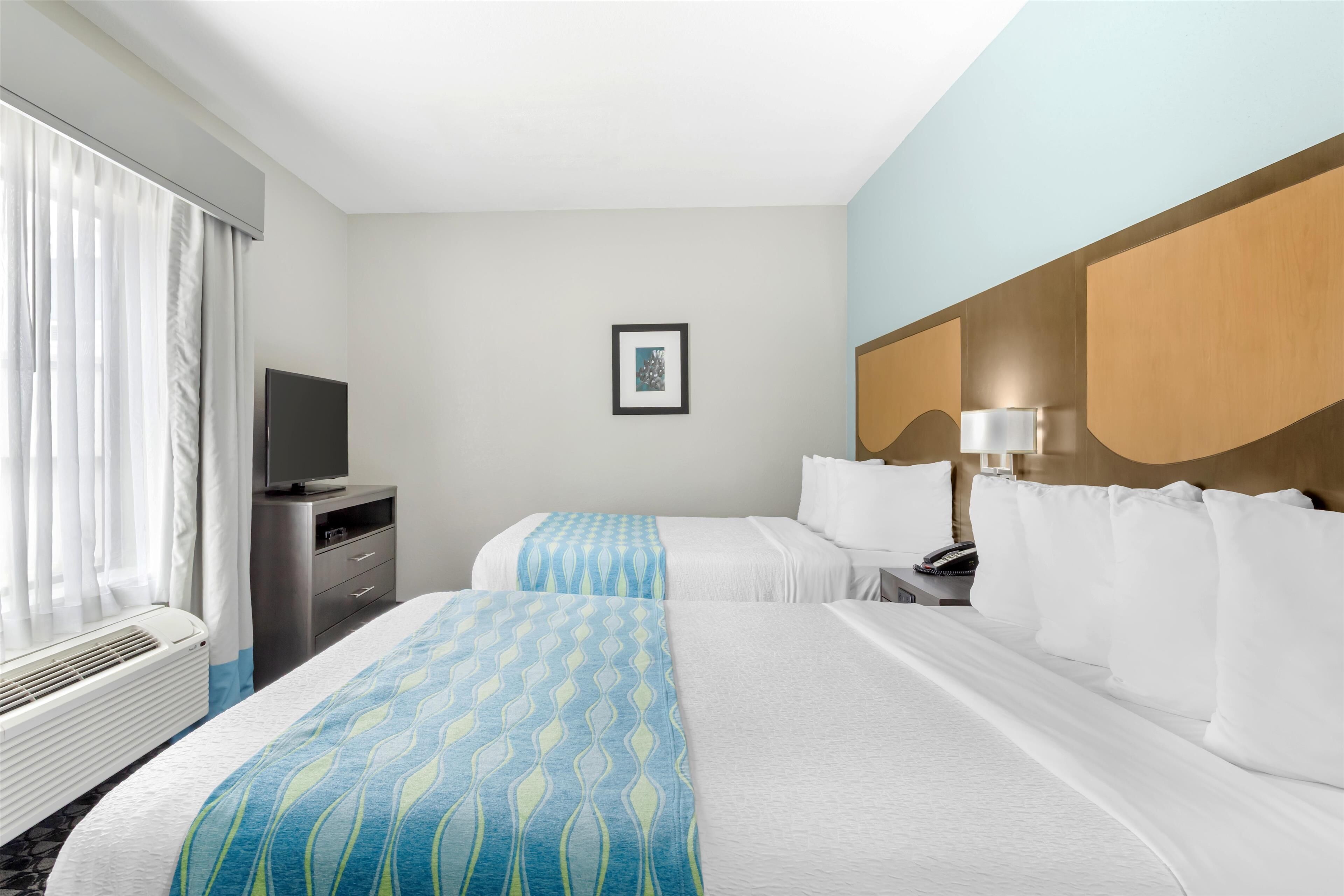 A hotel room with two beds, a TV, a desk, and a picture on the wall.