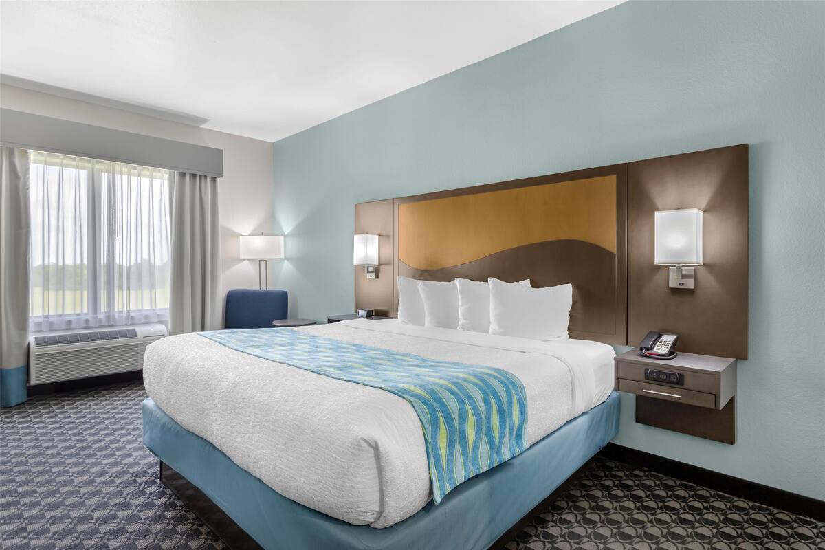 Habitación de hotel con una cama grande, dos lámparas de noche, una mesita de noche con un teléfono y una ventana con cortinas.