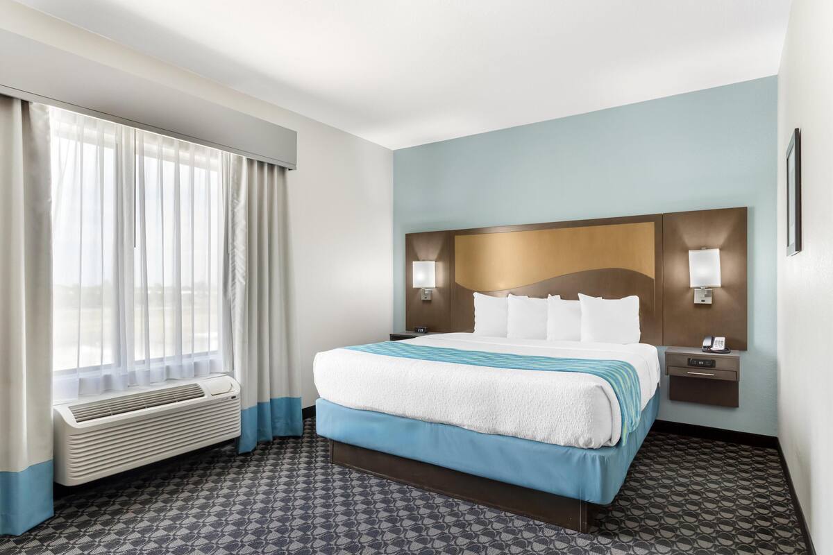 Habitación de hotel con una cama grande, una ventana con cortinas, una lámpara de pared y una mesita de noche con teléfono.