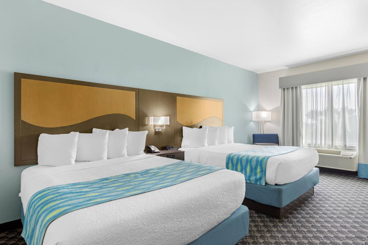 Habitación de hotel con dos camas, un cabecero grande sujeto a la pared, lámparas de noche, un teléfono y una ventana con cortinas.