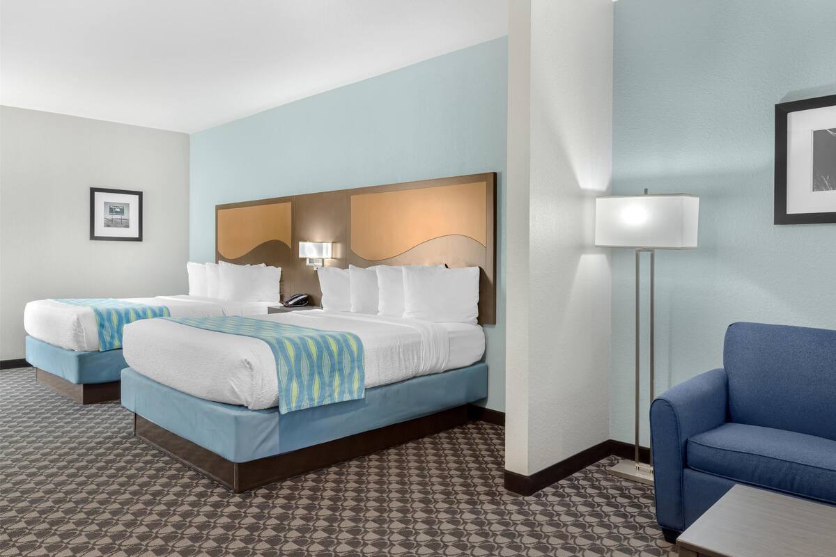 Una habitación de hotel con dos camas, un sofá azul, una lámpara y un cuadro en la pared.