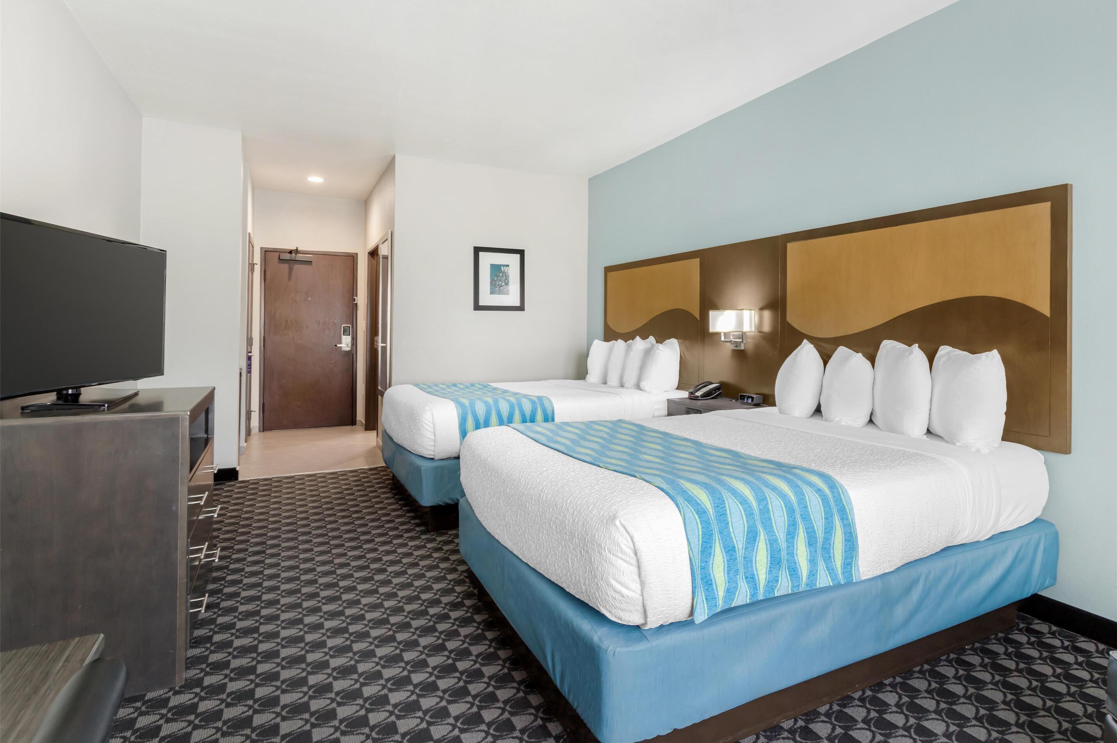 A hotel room with two beds, a TV, a desk, and a patterned floor.
