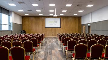 A conference room with rows of red chairs, a wooden panel wall, and a screen displaying 'GREENISLE HOTEL'.
