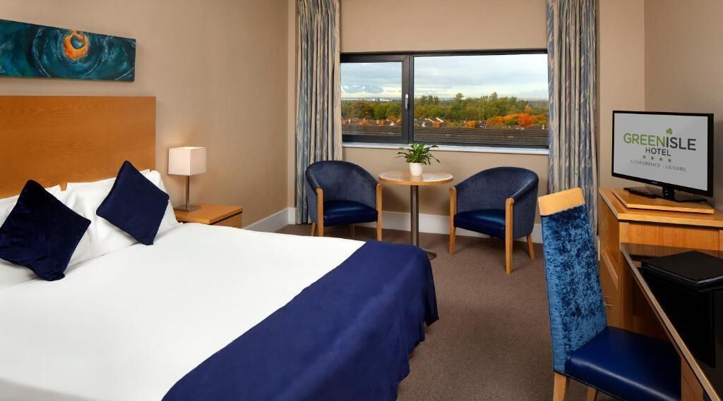 A hotel room with a bed, two chairs, a small table, a TV, and a view of the outdoors.