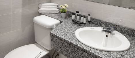 A modern bathroom with a white toilet, a granite countertop sink, and a glass shower enclosure.