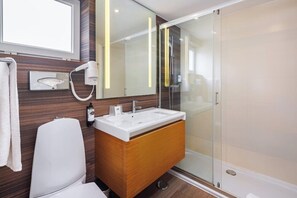 Un baño moderno con un lavabo blanco, tocador de madera y cabina de ducha de vidrio.