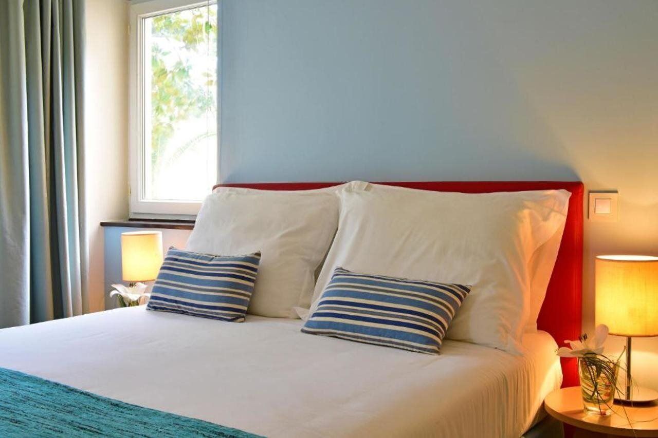 A hotel room with a bed, two pillows, a nightstand with a lamp, and a window with curtains.