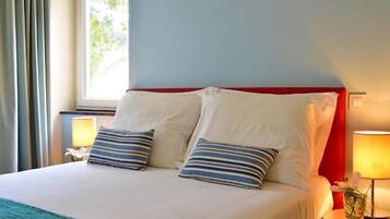 A hotel room with a bed, two pillows, a nightstand with a lamp, and a window with curtains.